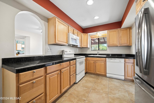 kitchen with light tile patterned flooring, light brown cabinets, white appliances, and sink