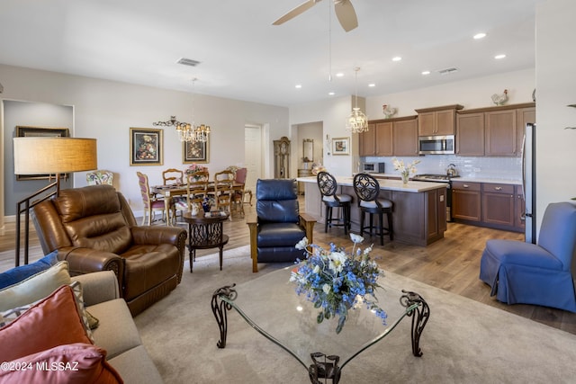 living room featuring ceiling fan with notable chandelier and light hardwood / wood-style flooring