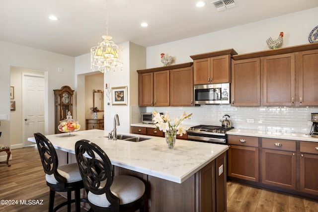 kitchen featuring a kitchen island with sink, stainless steel appliances, dark wood-type flooring, sink, and backsplash