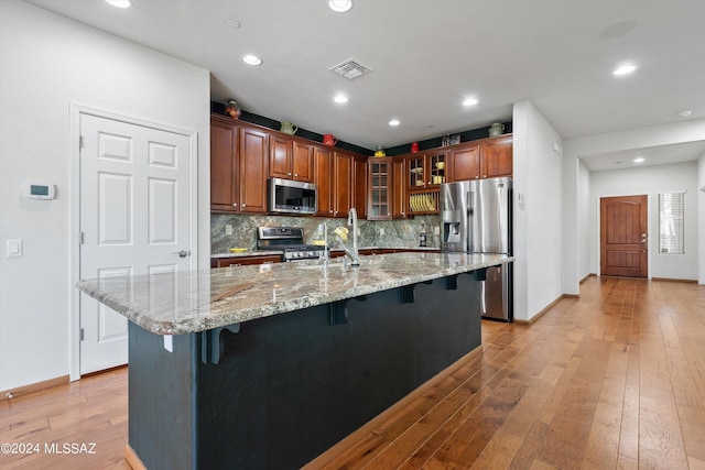 kitchen featuring visible vents, glass insert cabinets, appliances with stainless steel finishes, a breakfast bar, and a large island with sink