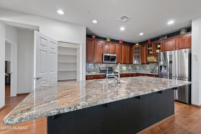 kitchen with stainless steel appliances, a spacious island, visible vents, glass insert cabinets, and a sink