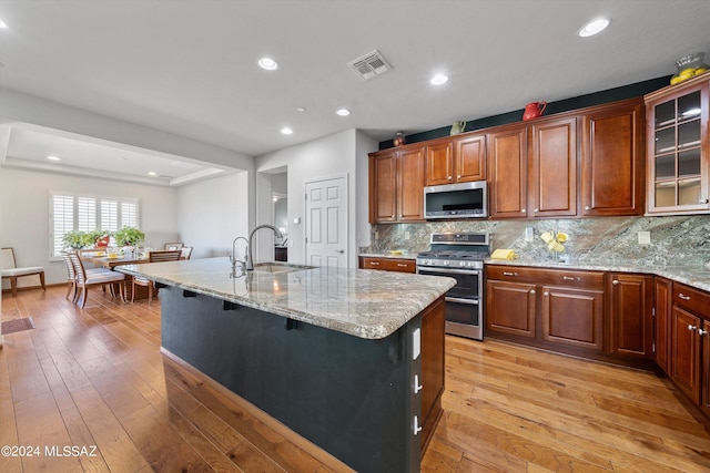 kitchen featuring a center island with sink, stainless steel appliances, visible vents, glass insert cabinets, and light wood-type flooring