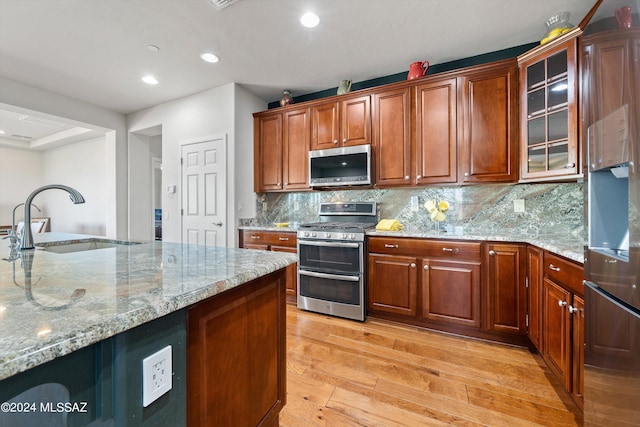 kitchen with stainless steel appliances, a sink, light wood-type flooring, light stone countertops, and glass insert cabinets