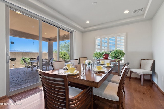 dining room with a raised ceiling, visible vents, and wood finished floors