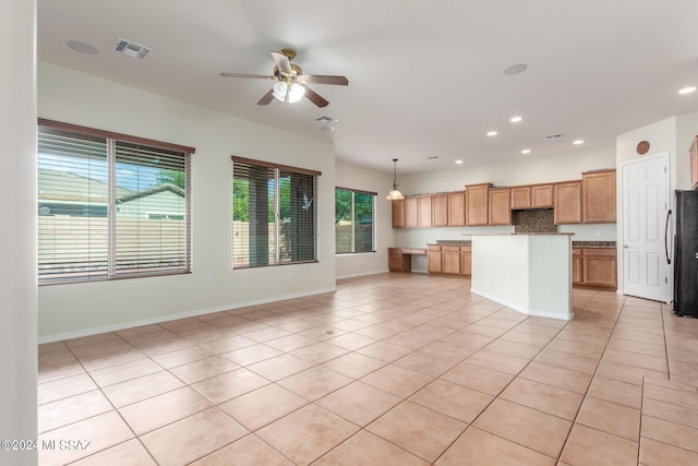 kitchen with light tile patterned floors, ceiling fan, black refrigerator, hanging light fixtures, and a kitchen island