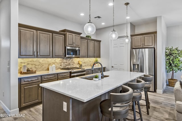 kitchen with sink, tasteful backsplash, a kitchen island with sink, appliances with stainless steel finishes, and light wood-type flooring