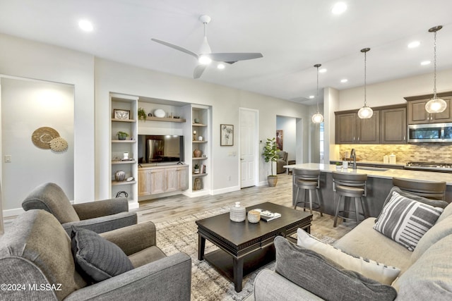 living room featuring built in features, light hardwood / wood-style flooring, ceiling fan, and sink