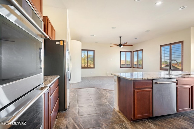 kitchen with light stone countertops, ceiling fan, sink, stainless steel appliances, and dark colored carpet