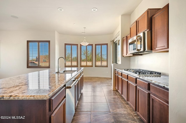 kitchen featuring light stone counters, stainless steel appliances, sink, hanging light fixtures, and an island with sink