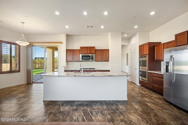 kitchen with pendant lighting, light stone countertops, stainless steel appliances, and an island with sink