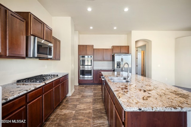 kitchen with light stone countertops, sink, a kitchen island with sink, dark tile patterned flooring, and appliances with stainless steel finishes