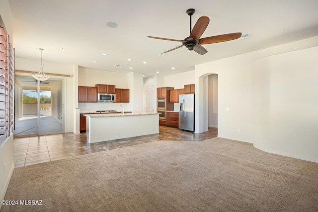 kitchen with a center island with sink, hanging light fixtures, sink, appliances with stainless steel finishes, and light colored carpet