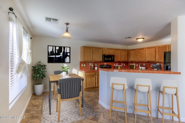 kitchen featuring decorative backsplash, hanging light fixtures, black appliances, and kitchen peninsula