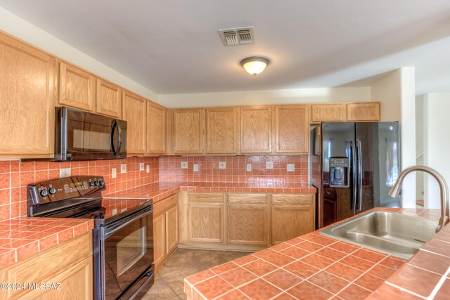 kitchen featuring black appliances, light brown cabinets, sink, tile countertops, and light tile patterned floors