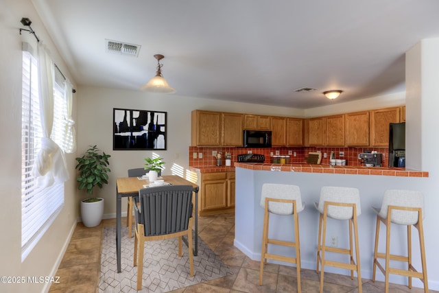 kitchen featuring black appliances, decorative light fixtures, tile counters, and tasteful backsplash