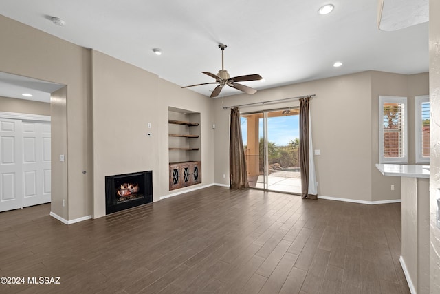 unfurnished living room with built in shelves, dark hardwood / wood-style flooring, and ceiling fan