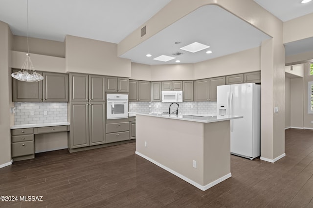 kitchen with tasteful backsplash, dark hardwood / wood-style flooring, white appliances, gray cabinets, and a center island with sink