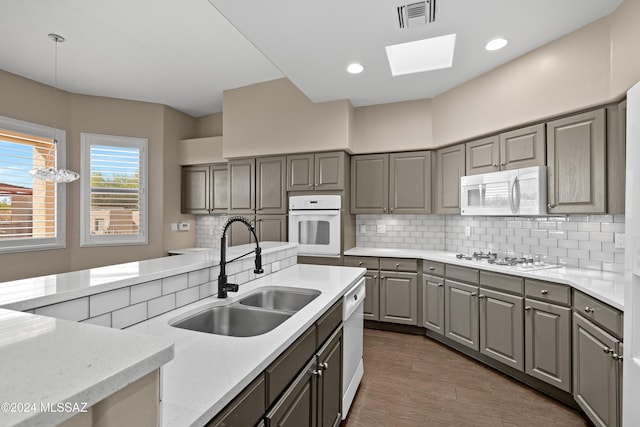 kitchen featuring a skylight, sink, decorative light fixtures, white appliances, and hardwood / wood-style flooring