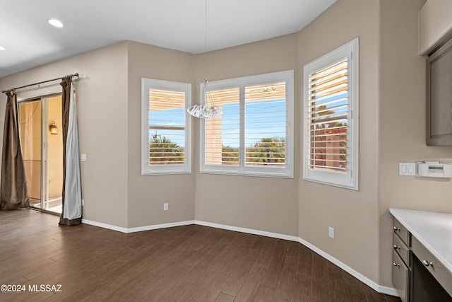 unfurnished dining area with dark hardwood / wood-style floors, a healthy amount of sunlight, and an inviting chandelier