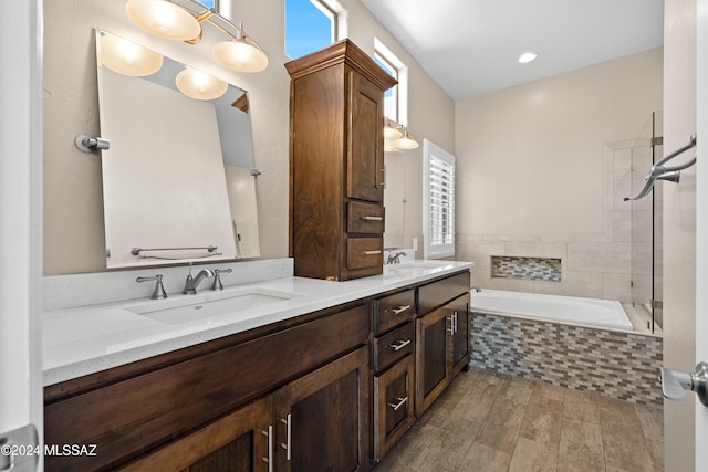 bathroom with wood-type flooring, vanity, and tiled tub