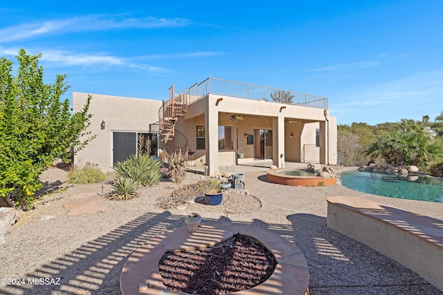 back of property featuring a balcony, ceiling fan, a swimming pool with hot tub, a fire pit, and a patio