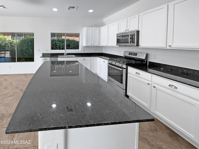 kitchen featuring a center island, dark stone counters, tile patterned flooring, white cabinetry, and stainless steel appliances