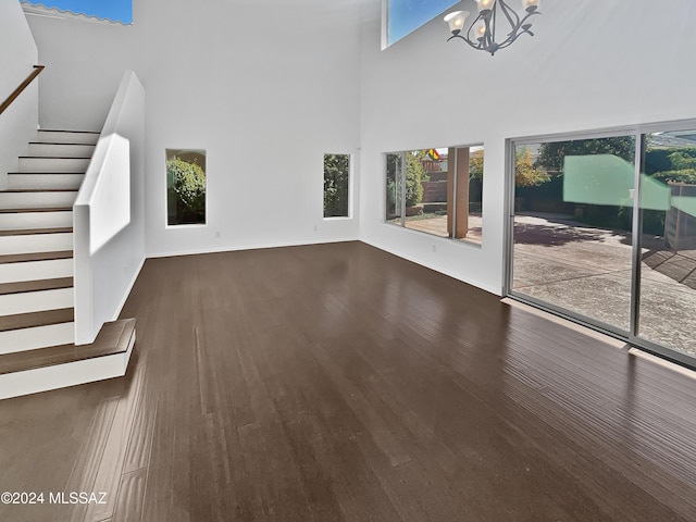 unfurnished living room featuring a towering ceiling, dark wood-type flooring, and an inviting chandelier