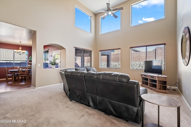 living room featuring ceiling fan with notable chandelier, carpet floors, and a high ceiling