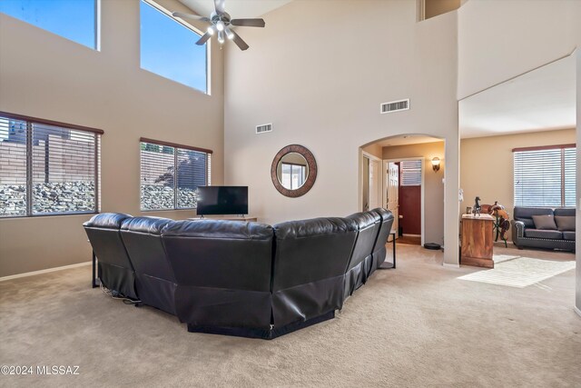 carpeted living room with a towering ceiling, a wealth of natural light, and ceiling fan