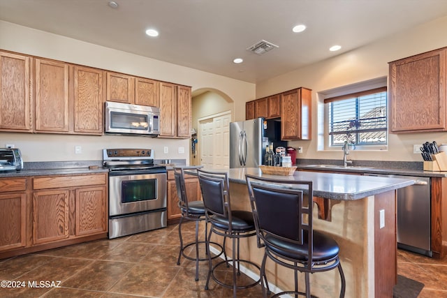 kitchen with a breakfast bar, stainless steel appliances, sink, dark tile patterned flooring, and a center island