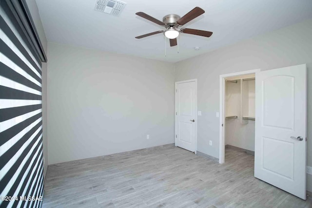 unfurnished bedroom with light wood-type flooring, a closet, a spacious closet, and ceiling fan