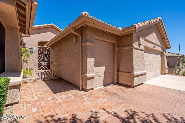 view of home's exterior with an attached garage, a tiled roof, decorative driveway, a gate, and stucco siding