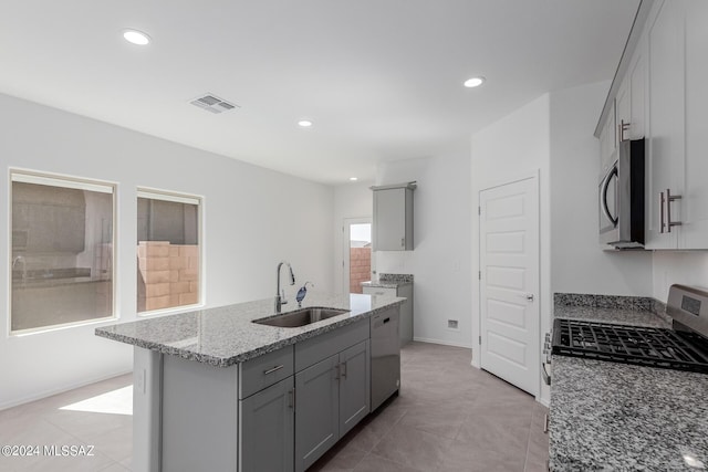 kitchen featuring sink, gas range, gray cabinets, an island with sink, and light stone counters