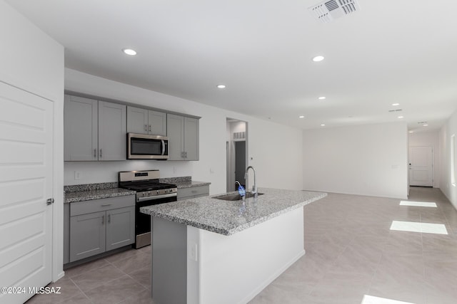 kitchen featuring appliances with stainless steel finishes, light stone counters, gray cabinetry, sink, and an island with sink