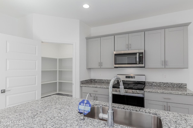 kitchen with light stone countertops, stainless steel appliances, gray cabinets, and sink