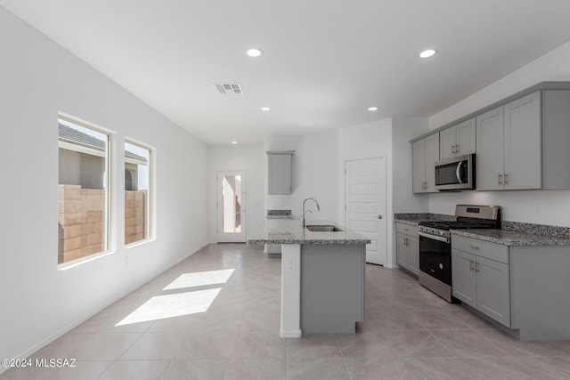 kitchen with gray cabinetry, sink, an island with sink, and stainless steel appliances