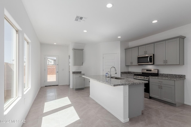 kitchen with appliances with stainless steel finishes, sink, gray cabinetry, and an island with sink