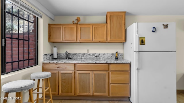 kitchen with white fridge, light stone counters, and sink