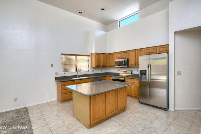 kitchen with a center island, sink, stainless steel appliances, a towering ceiling, and light tile patterned floors