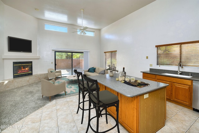 kitchen featuring a tile fireplace, ceiling fan, a center island, sink, and a kitchen bar