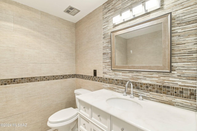 bathroom featuring decorative backsplash, vanity, toilet, and tile walls