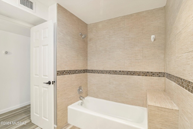 bathroom with tiled shower / bath, hardwood / wood-style flooring, and tile walls