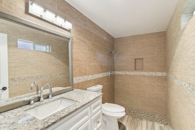 bathroom with vanity, toilet, tile walls, and a tile shower