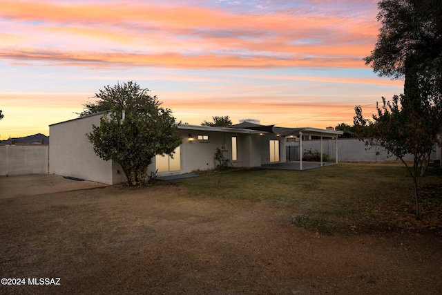 back house at dusk featuring a patio area and a yard