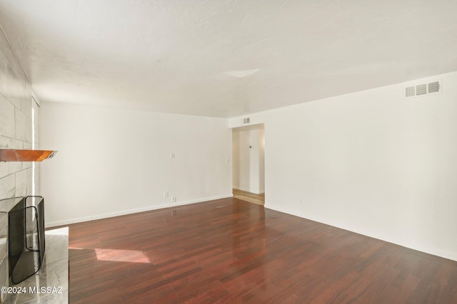 unfurnished living room with dark wood-type flooring and a tiled fireplace