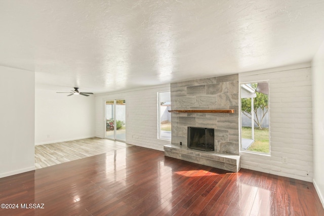 unfurnished living room with a stone fireplace, a healthy amount of sunlight, a textured ceiling, and hardwood / wood-style flooring