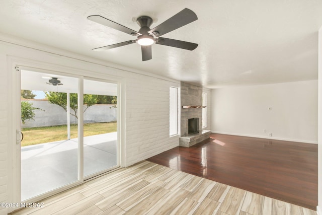 unfurnished living room with light wood-type flooring, a large fireplace, and ceiling fan