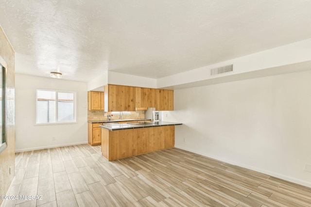 kitchen featuring light hardwood / wood-style floors, kitchen peninsula, backsplash, and black stovetop