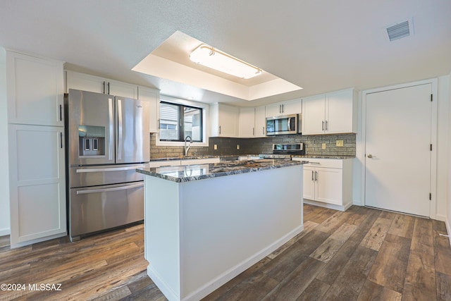 kitchen with dark wood-type flooring, dark stone counters, a tray ceiling, white cabinetry, and stainless steel appliances