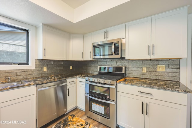 kitchen with white cabinets, appliances with stainless steel finishes, and dark stone counters